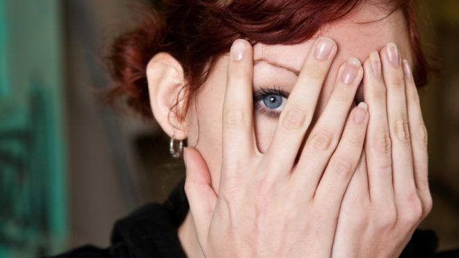 Woman peeking between fingers as she holds her hands in front of her face