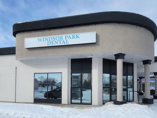 Windsor Park Dental building exterior, featuring a prominent sign indicating the dental practice's name. The structure has a modern design with large windows and is surrounded by snow, suggesting a winter setting.