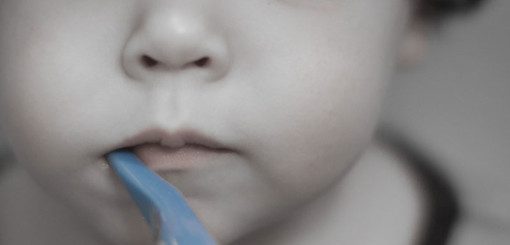 A close-up of a young child with a blue toothbrush in their mouth, highlighting their curious expression and playful innocence.