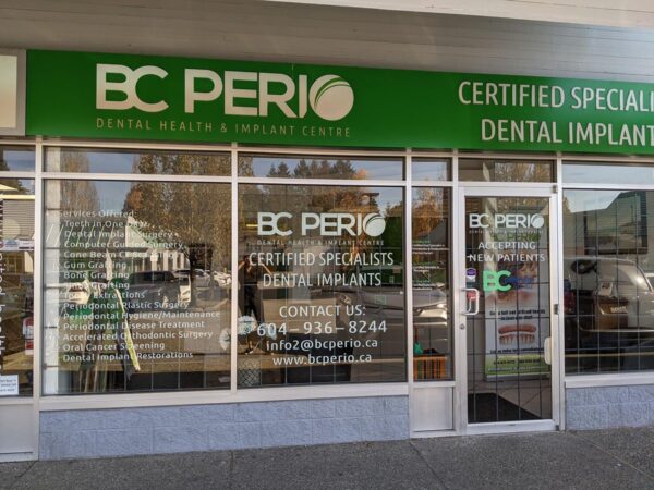 Exterior view of the BC PERIO dental clinic, showcasing large windows displaying the clinic's name, services as certified specialists in dental implants, and contact information. The building features a bright green sign and a clean, inviting entrance.
