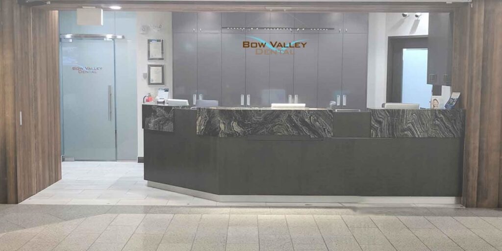 Modern office reception area with a sleek black desk, glass door on the left, and gray cabinets behind. The room has minimalistic decor and a clean, professional appearance.