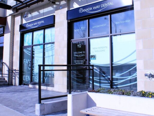 Exterior view of a row of modern business storefronts with large windows and a stone facade. Rails and steps lead up to the entrances, and a planter with greenery is visible in the foreground.