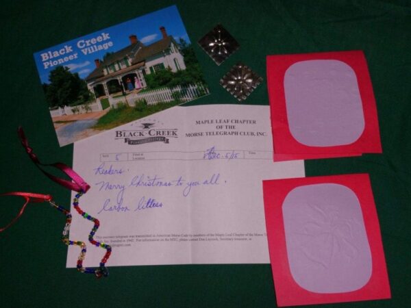 A collection of items arranged on a green surface, including a postcard from Black Creek Pioneer Village, a letter, two colorful blank cards, and decorative ribbon. The postcard features a historic building, while the letter expresses greetings.
