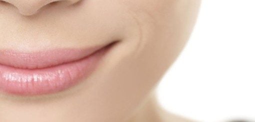 Close-up of a person's lips and chin, showing a subtle smile on a light background, highlighting the smoothness of the skin and natural contour of the lips.