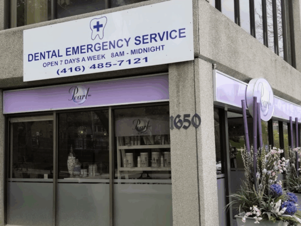 A dental emergency service clinic with a large sign, visible contact number, and purple decorative elements outside its entrance on a city street corner.