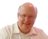 A smiling middle-aged man wearing glasses and a white collared shirt, seated at a table against a blurred background.