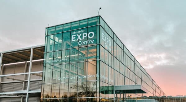 A modern glass building featuring a large sign that reads "EXPO Centre." The structure is set against a cloudy sky, reflecting a contemporary design.