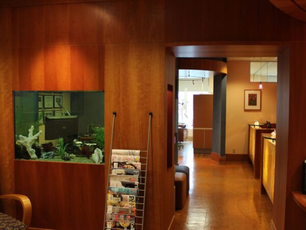 Wood-paneled room with a fish tank, magazine rack, and hallway leading to a softly-lit area in the background.