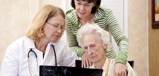A doctor and a woman assist an elderly woman as they look at a laptop together. The scene conveys care, support, and engagement in learning or sharing information.
