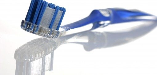 A close-up of a blue toothbrush with soft bristles, positioned at an angle. The toothbrush's handle is slightly curved, reflecting on a smooth surface.