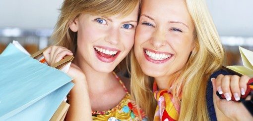 Two smiling young women embrace, holding shopping bags, exuding joy and friendship in a vibrant setting.
