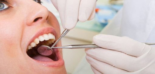 A dentist is examining a patient's mouth using dental tools while the patient has their mouth open, displaying their teeth. The scene takes place in a clinical setting, highlighting routine dental care.