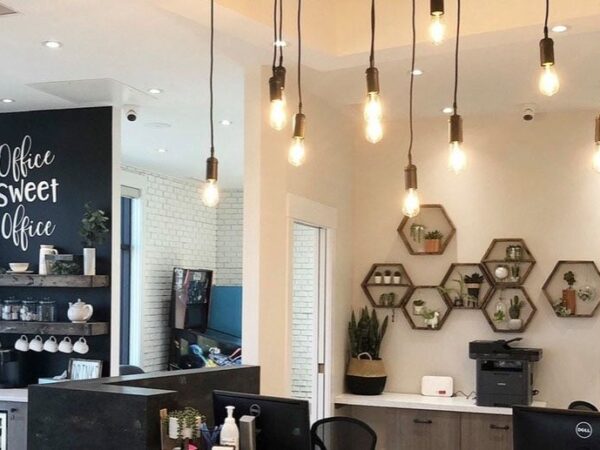 A modern office reception area featuring stylish pendant lights, a coffee station, and decorative wall art. The space is bright and inviting, with a contemporary design that combines functionality and aesthetic appeal.