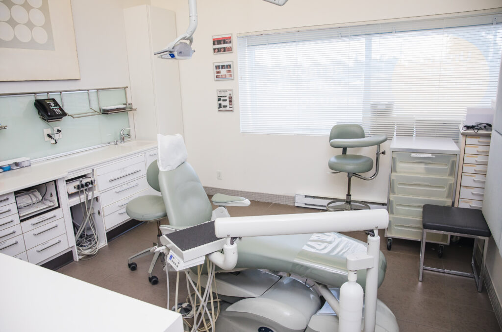 A dental office featuring a dental chair, a patient chair, and various dental equipment organized in a clean, bright space with natural light.