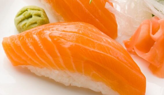 A plate featuring two pieces of salmon sushi, with vibrant orange fish atop white rice. Accompanied by wasabi, pickled ginger, and garnished with thin slices of green onion.