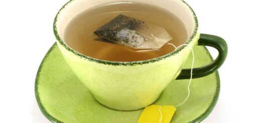 A green cup and saucer containing brewed tea with a tea bag steeping in the cup. A tag from the tea bag hangs over the edge.