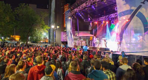 A large crowd gathers at night for a live music concert, with colorful stage lights illuminating the performers on stage.
