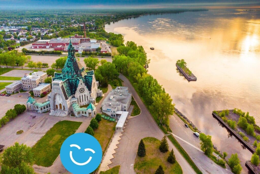 Aerial view of a riverside cityscape with a historic church, lush greenery, and a reflective waterway under a vibrant sky.
