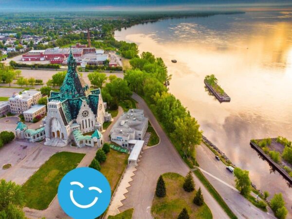 Aerial view of a riverside cityscape with a historic church, lush greenery, and a reflective waterway under a vibrant sky.