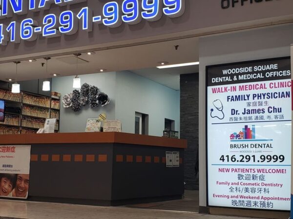Dental clinic entrance with bright signage displaying phone number. Reception area visible through large glass windows. Signs show information about medical services and contact details.