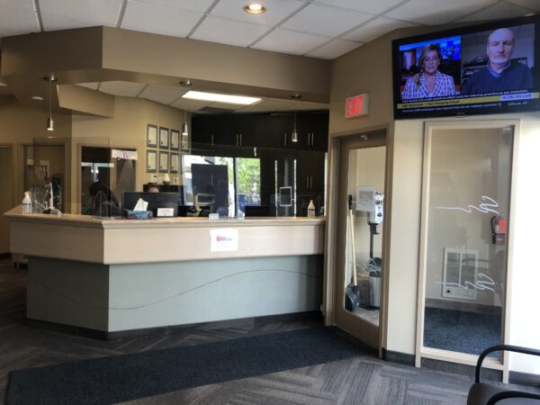 A modern dental office reception area featuring a welcoming front desk and comfortable seating. A television displaying news is mounted on the wall, contributing to a friendly atmosphere. The space is well-lit and organized, providing a pleasant environment for patients.