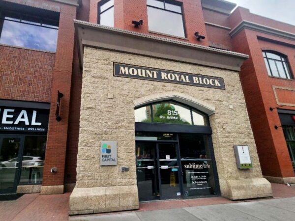 The image shows the entrance of the Mount Royal Block building, featuring a stone archway with the name prominently displayed. Adjacent storefronts are visible, contributing to a vibrant streetscape.