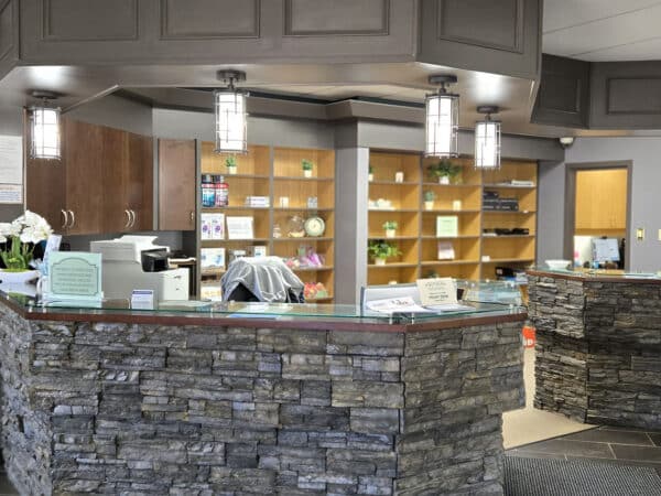 A modern dental office reception area featuring a stone counter, wooden shelves filled with brochures, and elegant lighting. A welcoming environment for patients with a clean, organized aesthetic.