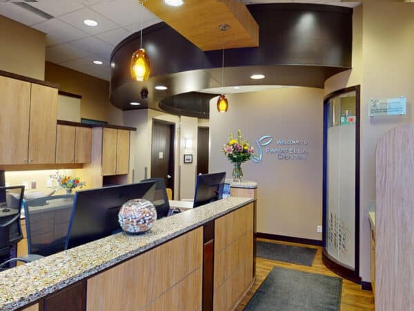 A modern dental office reception area featuring a warm color scheme and wooden finishes. The front desk is adorned with a floral arrangement and a friendly 123Dentist Smiley. Soft lighting enhances the inviting atmosphere, making it a welcoming space for patients.