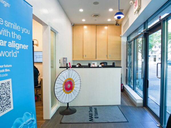 A dental office reception area featuring a blue promotional banner, a spinning prize wheel, a welcoming front desk, and large windows allowing natural light.