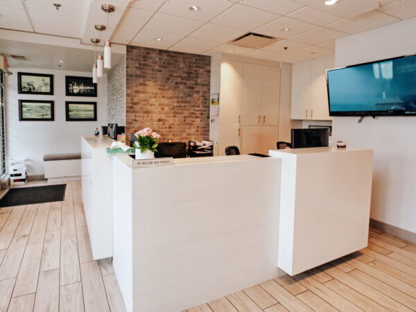 A modern reception area featuring a white desk, wooden flooring, and a stone wall. It includes a television screen and several framed pictures on the wall, creating an inviting atmosphere.