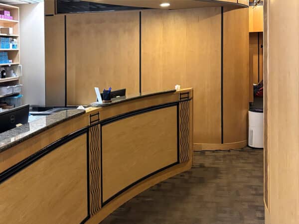 A warm dental office reception area featuring a curved wooden front desk, light-colored walls, and organized shelving. The inviting space is designed to create a welcoming atmosphere for patients, complemented by the cheerful presence of the 123Dentist Smiley nearby.