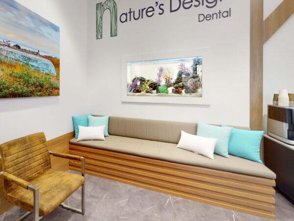 A modern dental office waiting area featuring a wooden bench with cushions, an art piece of a landscape on the wall, and a small aquarium, creating a calming atmosphere.