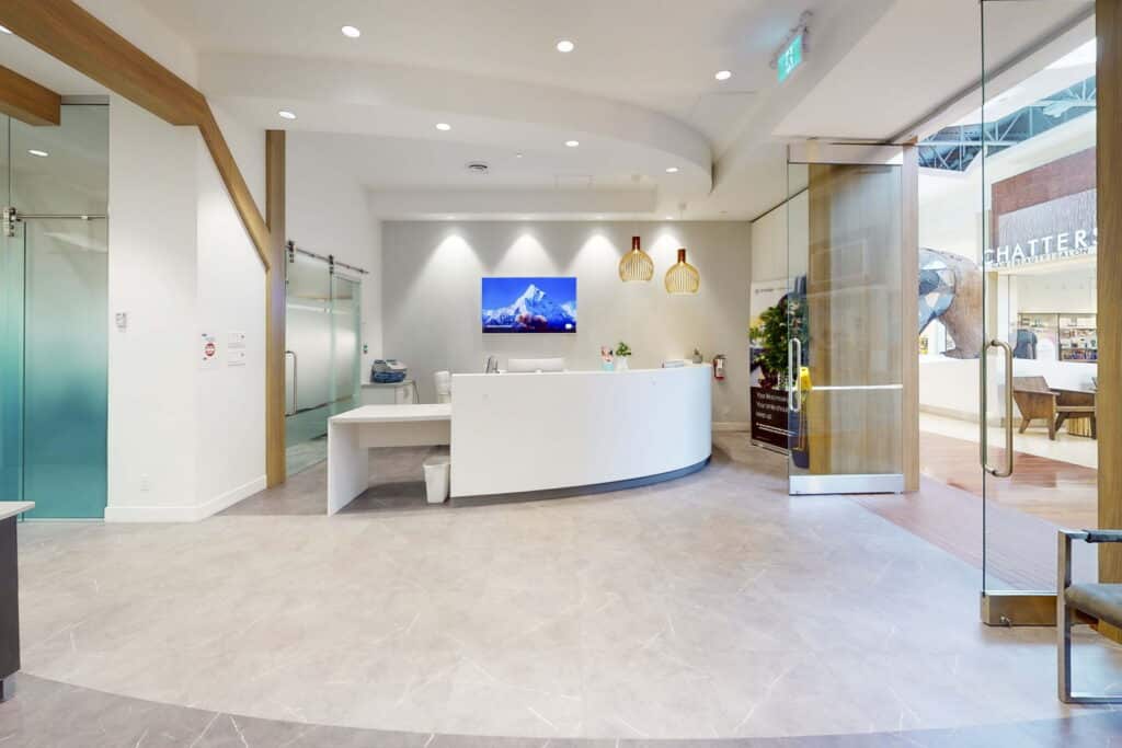 Modern reception area featuring a curved desk, wall-mounted television, soft lighting, and glass walls, creating a welcoming and open atmosphere.