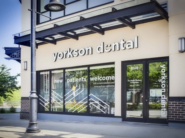 Exterior of Yorkson Dental office featuring a modern design, large windows displaying "new patients welcome," surrounded by greenery and a lamp post nearby.