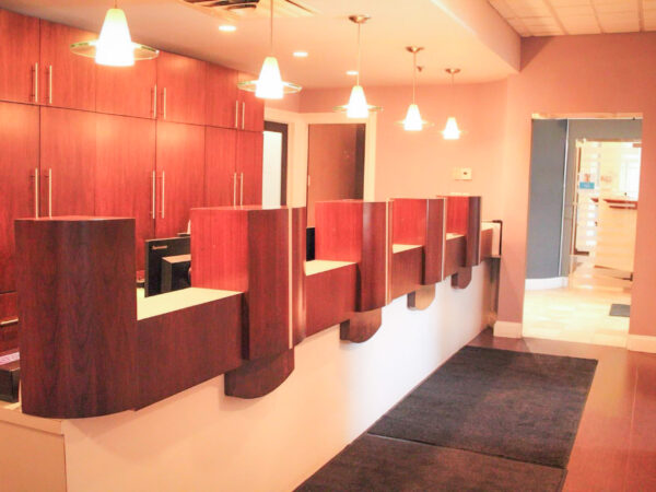 A welcoming dental office reception area with wooden countertops, soft lighting, and a clean, organized space. The entrance is visible, offering an inviting atmosphere for patients.