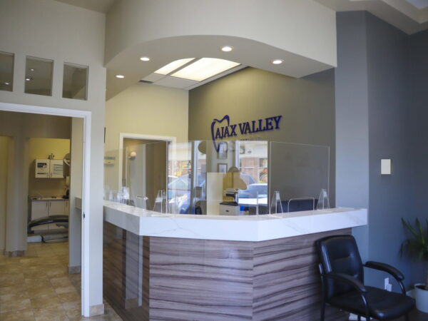 An interior view of a modern reception area featuring a counter with a protective barrier, a comfortable chair, and the name "VALLEY" displayed on the wall. The space is well-lit with neutral colors and contemporary design elements, creating an inviting atmosphere.