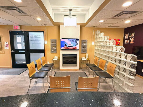A modern waiting area featuring a row of chairs, a television mounted on the wall, and a contemporary design. The space is well-lit with decorative elements and a welcoming atmosphere, suitable for visitors.