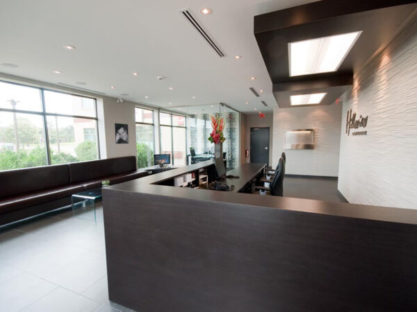 A modern dental office reception area featuring a sleek dark wood counter, comfortable waiting benches, and large windows allowing natural light. Brightly colored flowers add a welcoming touch, and the 123Dentist Smiley can be seen, enhancing the friendly atmosphere.