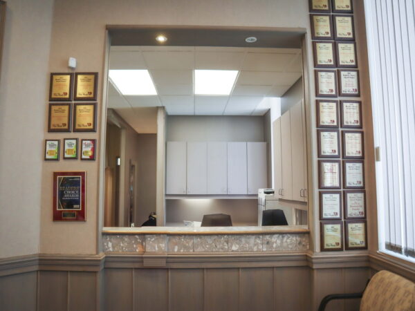 An interior view of an office reception area featuring a service counter, several framed certificates on the walls, and a clean, organized backdrop. The space is well-lit, emphasizing a professional atmosphere.