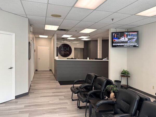 A modern dental office featuring a reception desk, comfortable seating, and a television displaying news. The interior is well-lit, with neutral colors and a tidy appearance, creating an inviting atmosphere for patients. The friendly 123Dentist Smiley adds a touch of warmth to the environment.