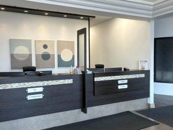 A modern reception area featuring two dark wood front desks, minimalistic decor, and abstract circle artwork on the wall. The space is bright with a clean, welcoming atmosphere, suitable for a professional setting.