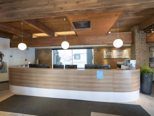 A modern reception area featuring a wooden front desk, large windows, and stylish lighting. The space includes a plant and showcases a friendly atmosphere, ideal for welcoming visitors.