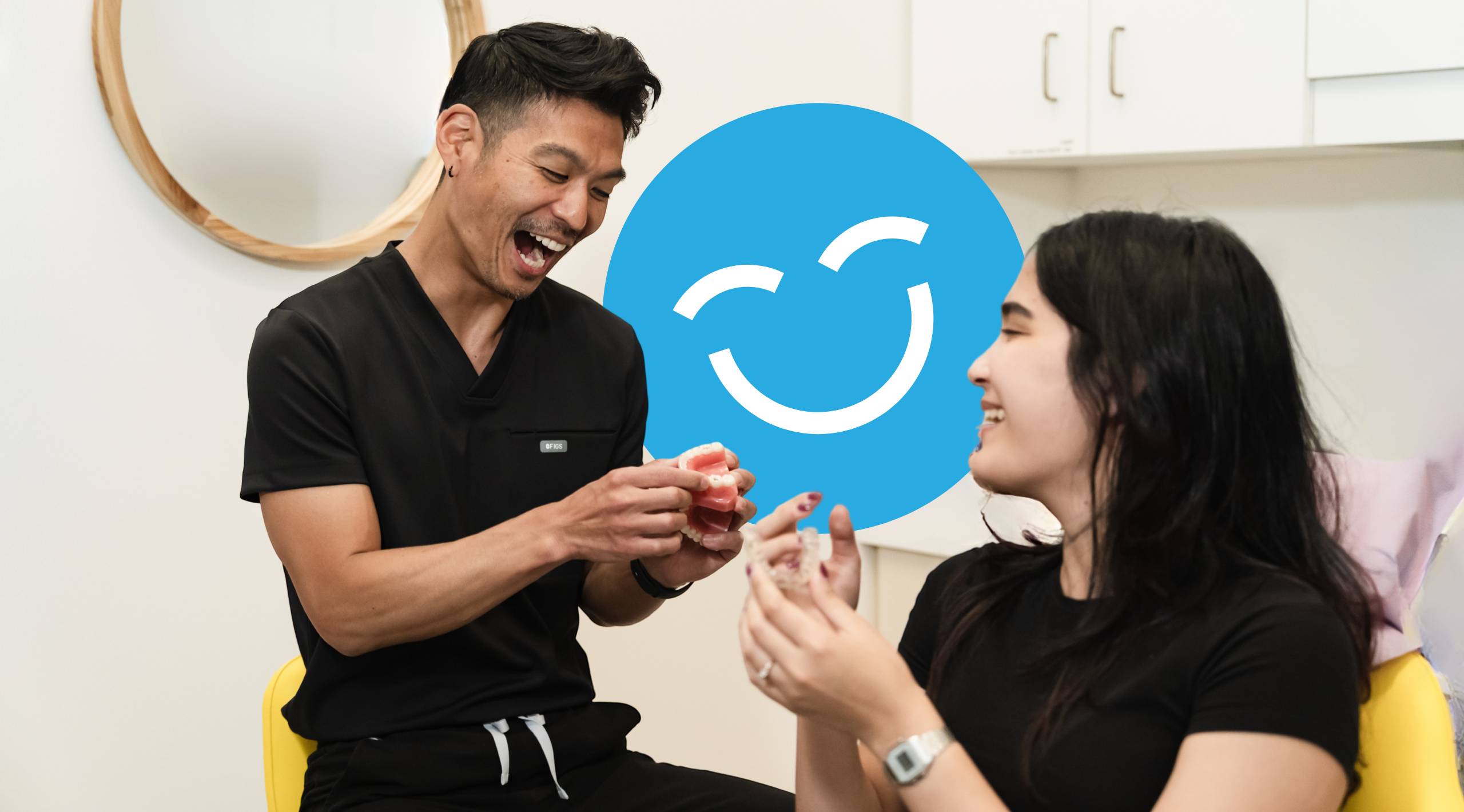 A dental professional engages with a patient in a friendly manner, showcasing a playful interaction. The 123Dentist Smiley is prominently featured, reflecting a welcoming and cheerful atmosphere in a dental setting.
