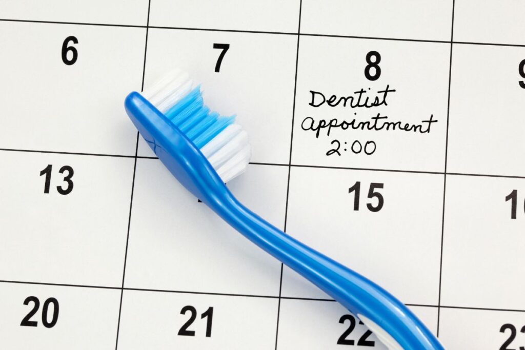 A blue toothbrush rests on a calendar date marked for a dentist appointment at 2:00. The image emphasizes dental care and reminds viewers of the importance of regular check-ups.