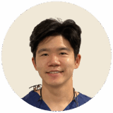 A smiling male dentist wearing blue scrubs, with dark hair and a cheerful expression. The background is neutral, emphasizing his friendly demeanor and professional appearance.