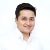 A smiling person in a white shirt poses against a plain background, exuding warmth and approachability.