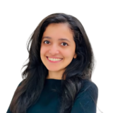 A person with long dark hair is smiling warmly at the camera, wearing a black top against a plain white background.