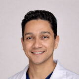 Smiling person wearing a white coat, set against a plain background.