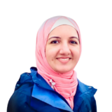 A woman wearing a light pink hijab and a blue jacket smiles warmly against a white background.