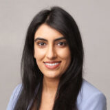 A person with long dark hair and a friendly smile, wearing a light-colored blazer, against a plain background.